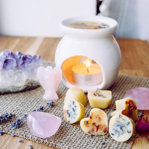 Homemade mini wax melts in aromatherapy lamp diffuser at home interior with rose quartz crystal hearts and angel for decoration on wooden window sill on winter. Seasonal spiritual zen concept.